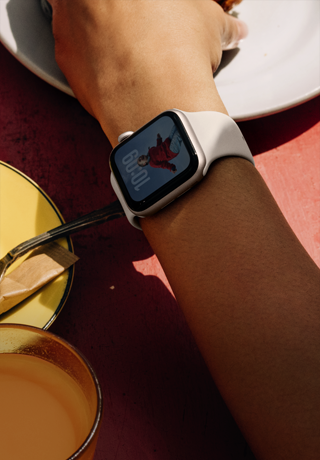 Bileğinde Yıldız Işığı renkte alüminyum kasaya sahip Apple Watch SE 3 takılı bir kişi kahvaltılıklara uzanıyor, hep açık ekran, kadranda bir kişinin fotoğrafı, yıldız ışığı renkte Spor Kordon