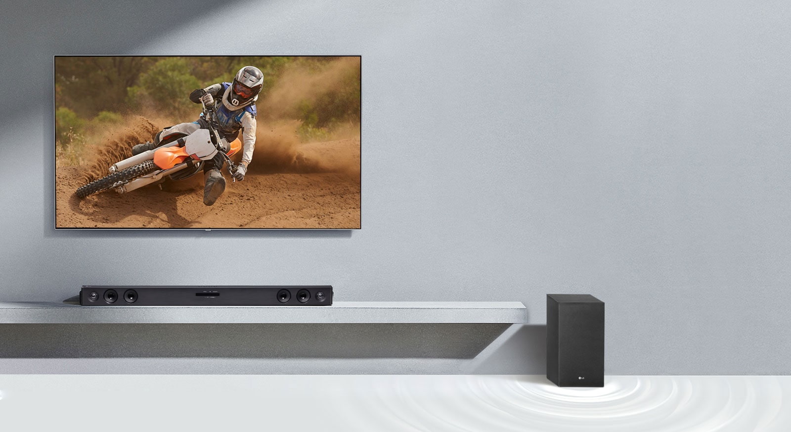 LG Soundbar SQC2 ve LG TV, oturma odasına birlikte yerleştirilmiştir. Subwoofer, soundbar'ın yanına yerleştirilmiştir. Açık TV'de motosiklet görüntüsü gösterilir.