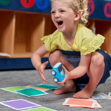 Child smiling and holding indi learning robot for kids.