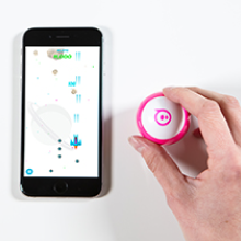 Telefondaki bir atari oyununun yanında oyun kumandası olarak Sphero Mini robot oyuncağını kullanan el.