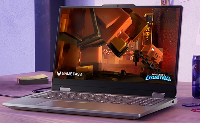 Masa üzerinde Lenovo LOQ Essential 15IRX11 dizüstü oyun bilgisayarı - önden görünüm, kapak açık, ekranda Minecraft Legends ekranı ve PC Game Pass logosu.