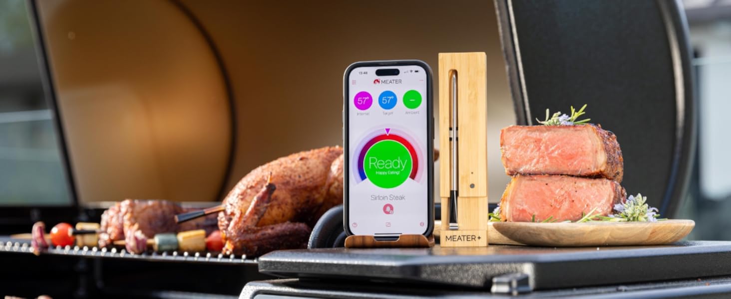 Kesme tahtası üzerinde ızgara etin yanında renkli dairesel göstergeler bulunan bir pişirme uygulamasını gösteren akıllı telefon.