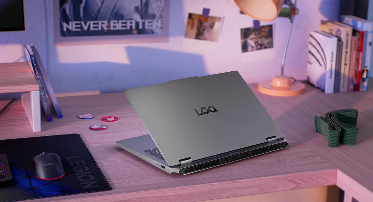 Lenovo LOQ Essential 15IRX11 dizüstü oyun bilgisayarı, fare, klavye, mousepad ve monitör ile masa üzerinde - arkadan görünüm, kapak kısmen açık.