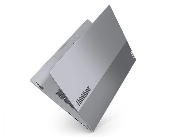 Sağ ön köşesine yaslanmış ve üst kapağındaki ThinkBook kimliğine odaklanan, kapağı neredeyse tamamen kapalı şekilde duran Lenovo ThinkBook 14 Gen 7 dizüstü bilgisayarının havada süzülen görüntüsü.