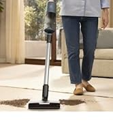 Ahşap zemin üzerinde kullanılan ayaklı elektrikli süpürge, modern bir oturma odasında görünür mobilya ve bitkiler.