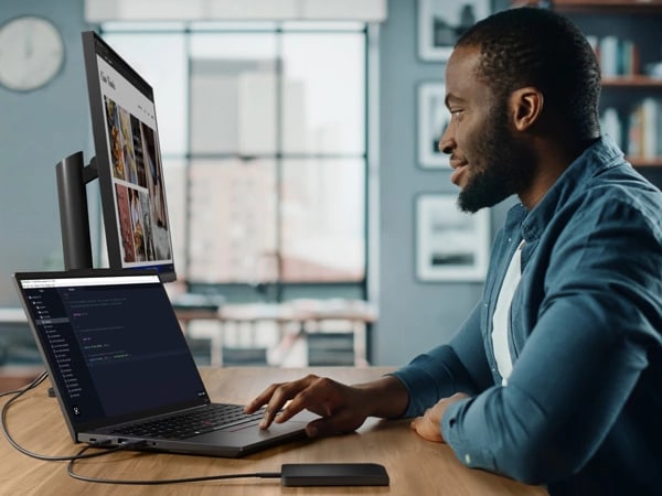 Person sitting at desk in home studio, facing ThinkPad E14 Gen 5 (14" Intel) laptop and using trackpad to navigate files