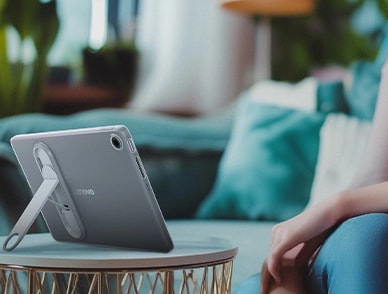 Lenovo Tab, arka planda rahat bir oturma odası ortamı ile stand modunda bir masanın üzerine yerleştirilmiştir.