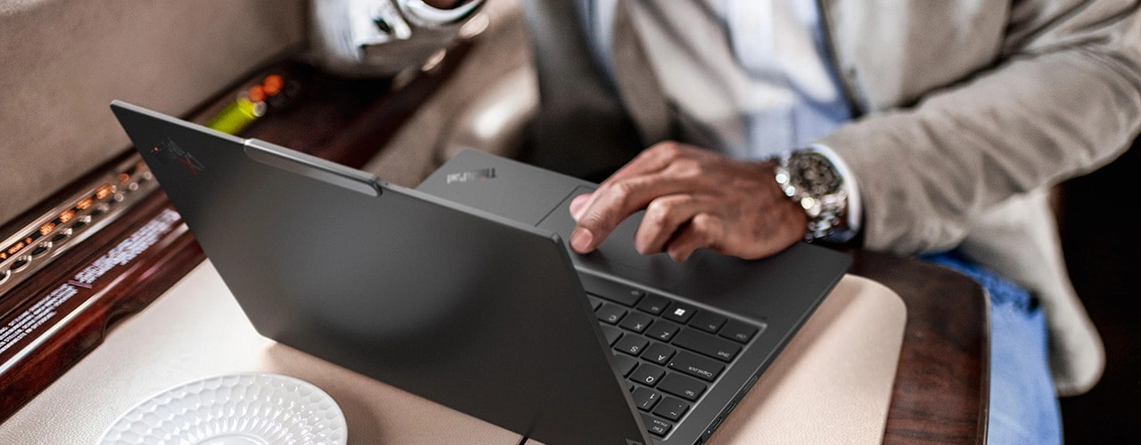 Overhead shot of a person on a train using the Lenovo ThinkPad X1 Carbon Gen 12 laptop, on a table.