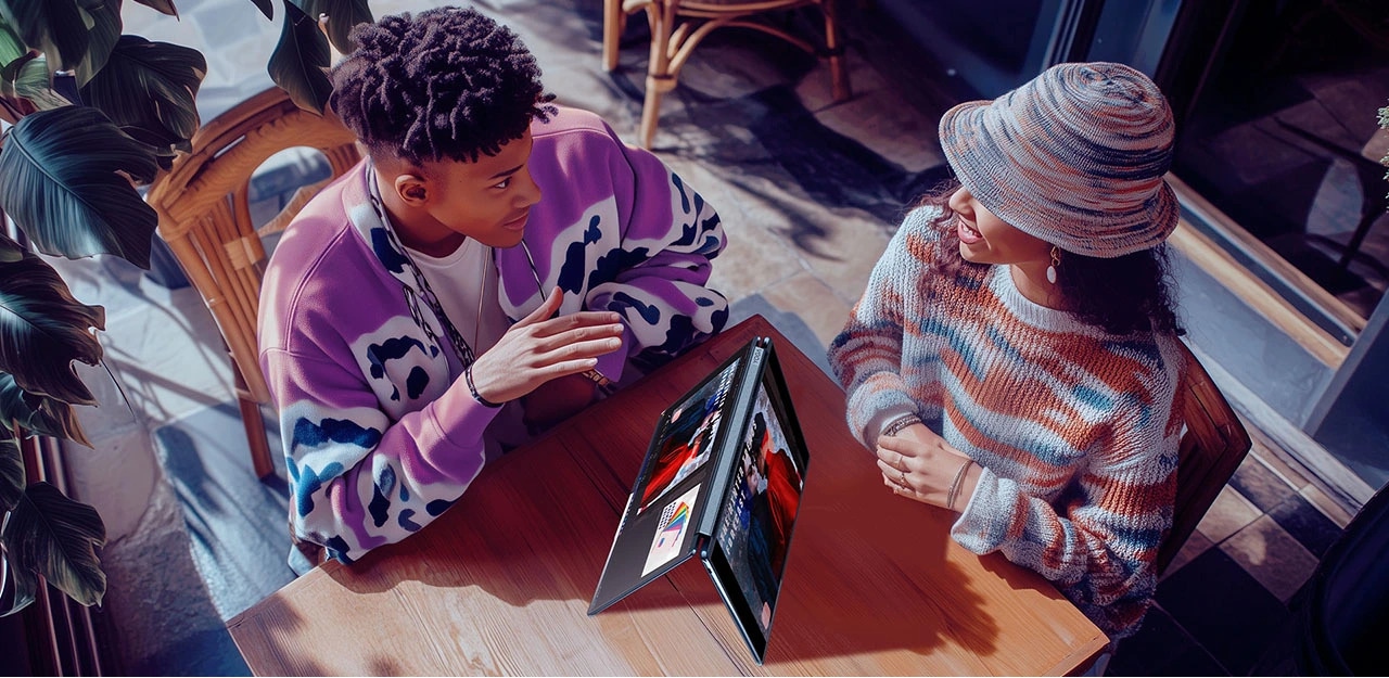 Aerial view of two young people having a discussion in a café environment with a Yoga Book 9i in tent mode between them.