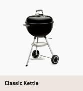 Metin şöyledir: 'Classic Kettle'. Siyah küre şeklinde ayaklı ve tekerlekli kömür mangalı, beyaz arka planda resmedilmiştir.