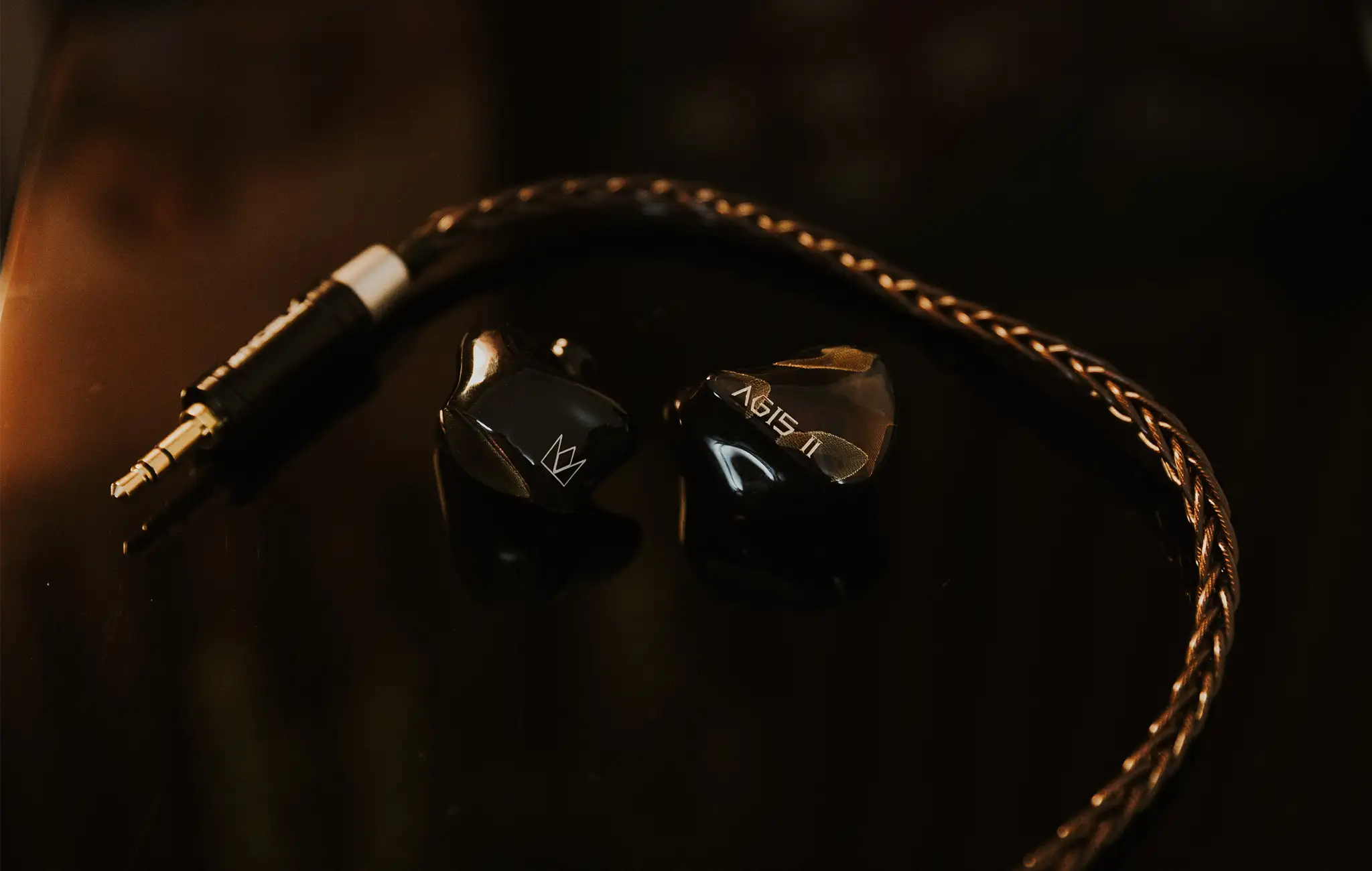 Noble Audio Agis II IEMs closeup sitting on top of black floorstanding speaker with orange lighting hue and cable lying around