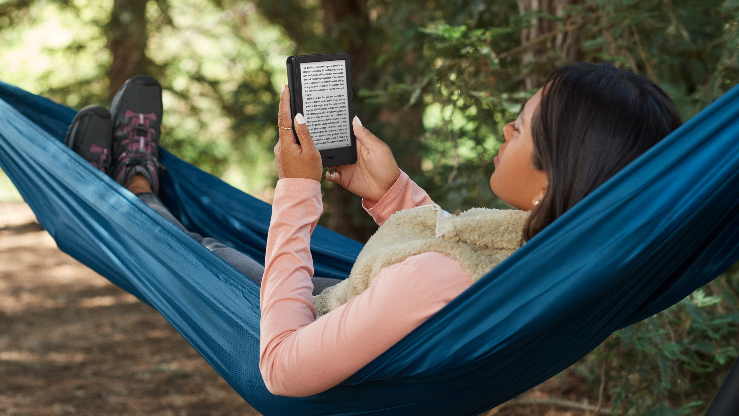 Kadınlar dışarıda hamakta uzanmış Kindle'da kitap okuyorlar.