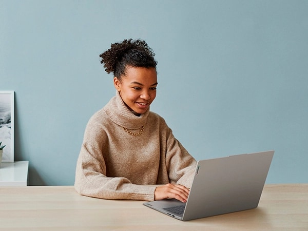 Masa üzerine yerleştirilmiş Artic Grey renkli Lenovo IdeaPad Slim 3i Gen 9 16 inç dizüstü bilgisayarda evde çalışan bir kişinin önden görünümü. Görüntü dizüstü bilgisayarın arka görünümüne odaklanıyor.