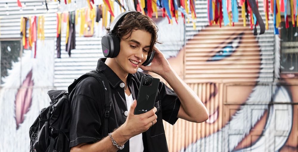 Yüksek kaliteli gaming kulaklık ve akıllı telefon kullanıcısı, şehir sokaklarında grafiklerle süslenmiş graffiti duvar önünde eğlenceli ve rahat gaming deneyimi yaşıyor.