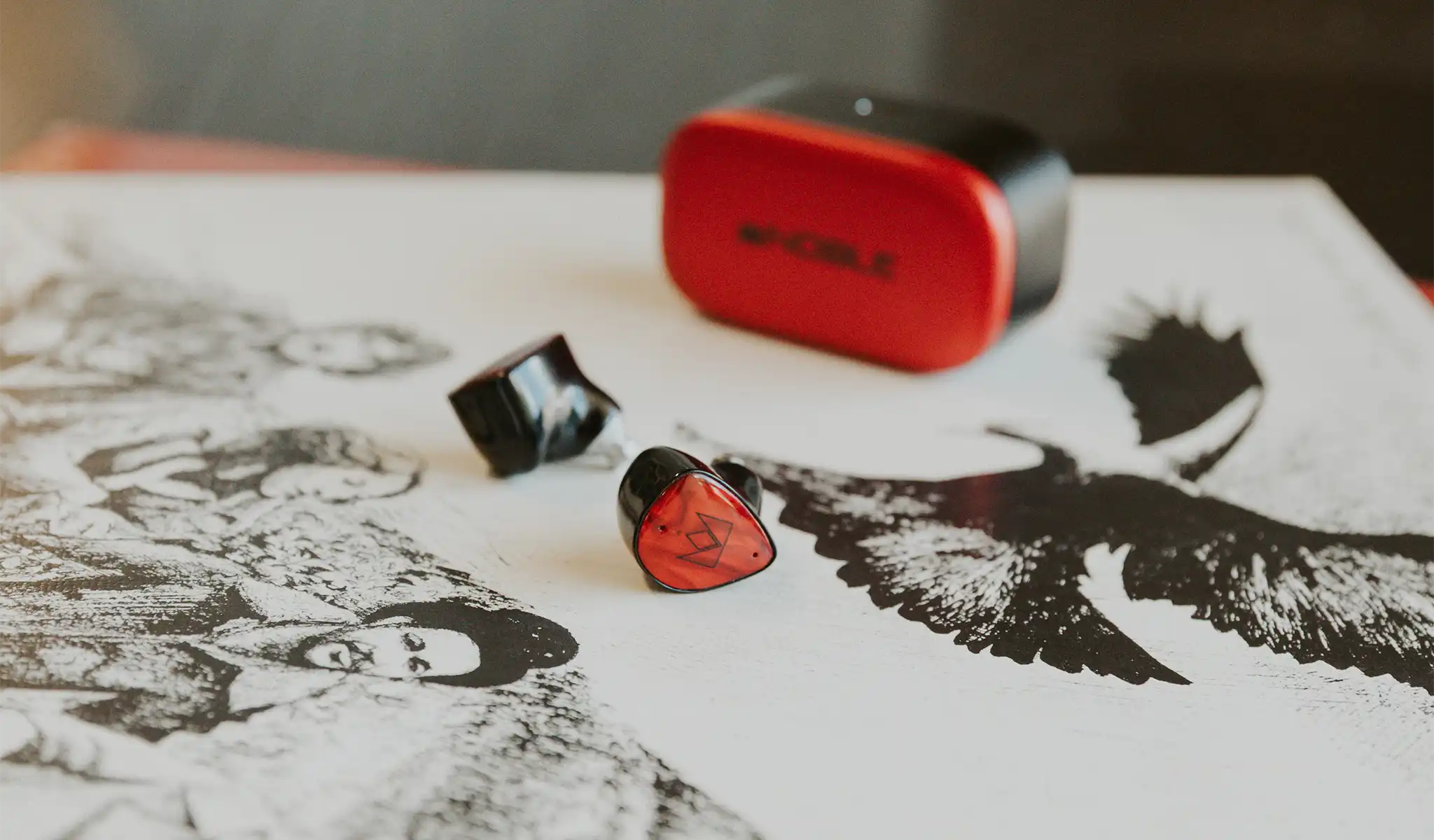 Noble Audio FoKus Amadeus earphones front and rear view with charging case behind sitting on vinyl record on black wooden table