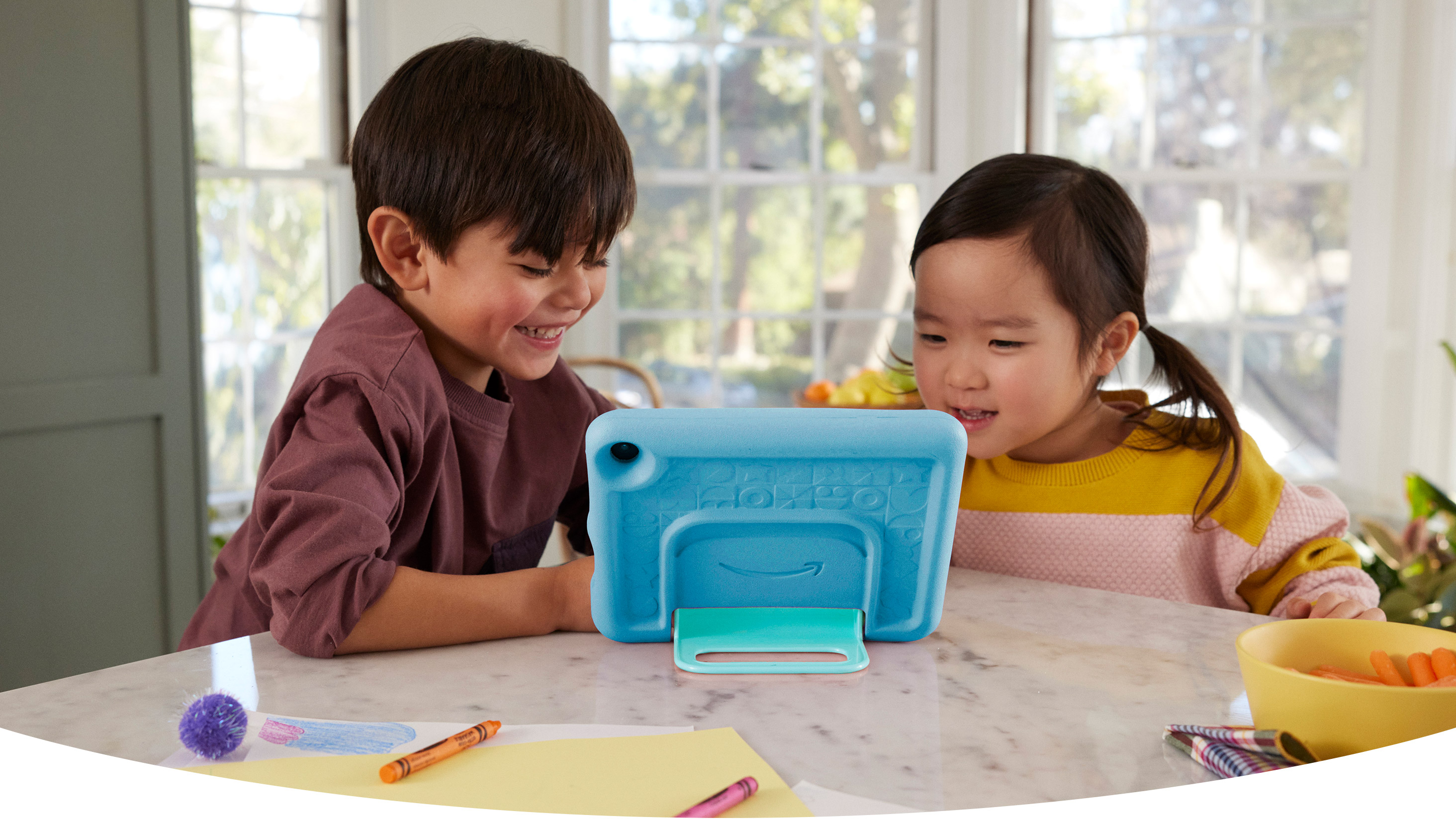 İki küçük çocuk gülümsüyor ve sağlam bir kutunun içinde bir standın üzerinde duran Fire HD 8 Kids'i izliyor.