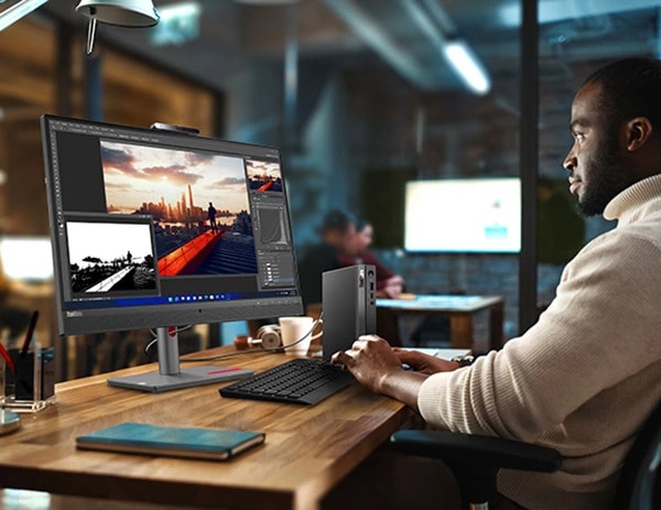 Bir ofis masasında, monitör ve klavyenin (ayrı satılır) yanında dikey olarak duran Lenovo ThinkCentre Neo 50q Gen 4 (Intel) Tiny'nin yan görünümü, klavyede yazan bir kişiyle birlikte