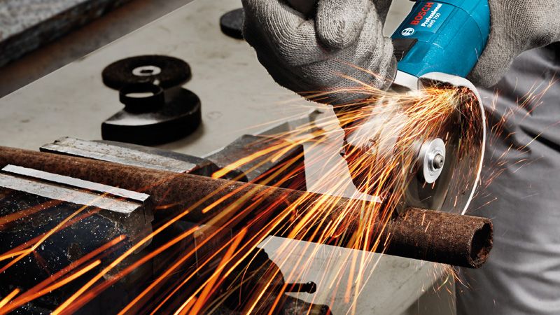 Güvenlik ekipmanı takan bir kişi, açılı taşlama makinesiyle paslanmış bir metal boruyu taşlıyor.
