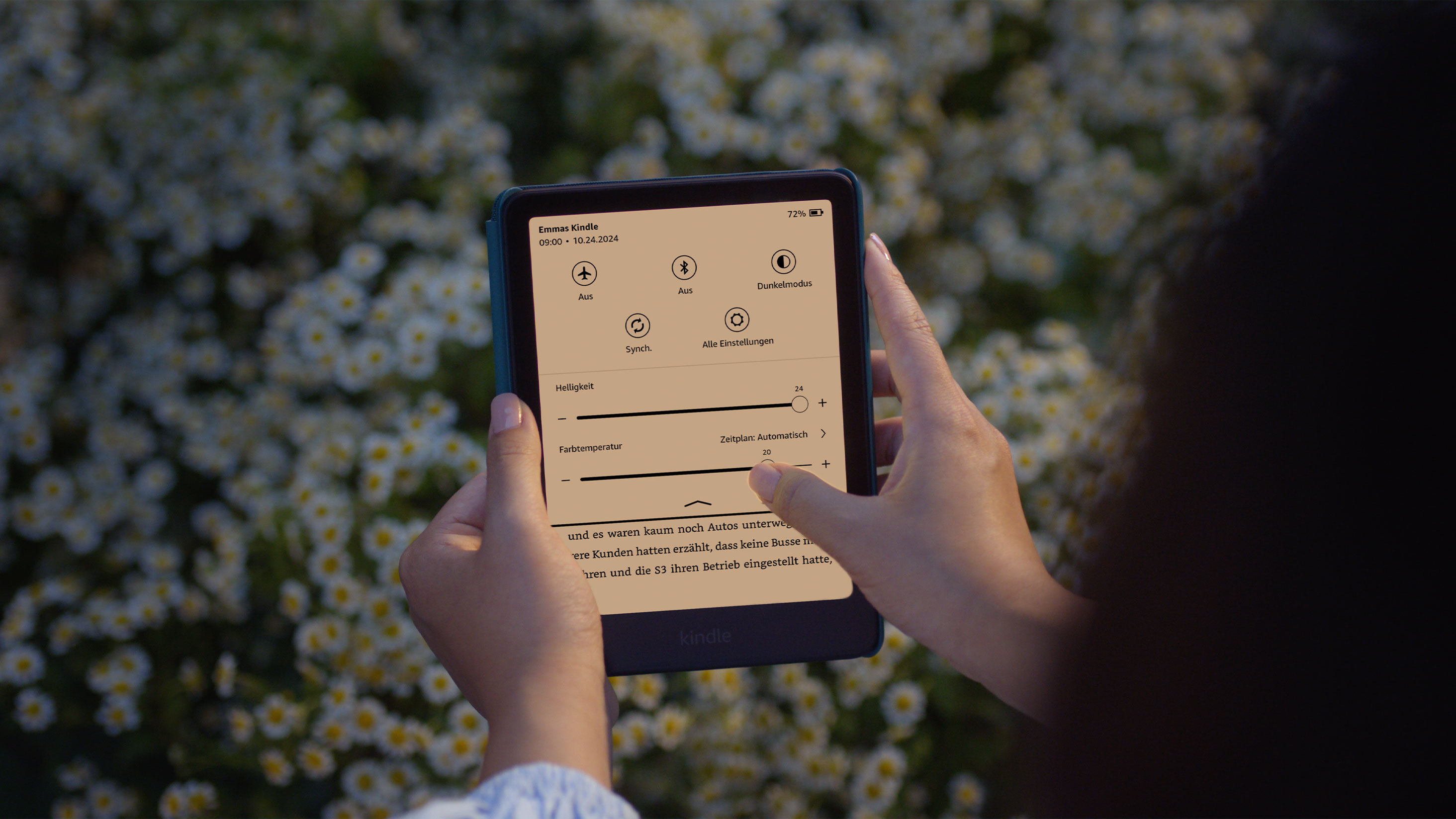 Çiçek tarlasında bir kadın Kindle'ında kitap okuyor. Ekranın parlaklığını ve renk sıcaklığını ayarlıyor.