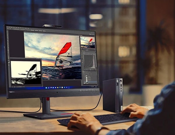 Lenovo ThinkCentre Neo 50q Gen 4 Tiny (Intel), bir ofis masasının üzerinde, monitör ve klavyenin (ayrı satılır) yanında, klavyede yazan bir kişiyle birlikte dikey olarak duruyor