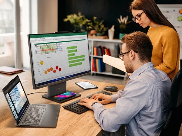 Bir masada oturan ve Lenovo ThinkCentre Neo 50a Gen 5 24 inç Intel monitörde verilerle çalışan iki kişi, bir Lenovo dizüstü bilgisayar ve kablosuz klavye ve fare kullanıyor